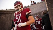 Harvard football player in red jersey 51 walks out of tunnel onto field with teammates behind.