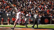 Harvard football player in a white uniform runs towards the end zone, with a cheering crowd in the background.
