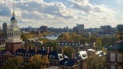 Skyline view of Harvard University with trees in autumn colors and a river under a cloudy sky.