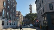 A person walks across a street lined with historic buildings and a clock tower in the background.