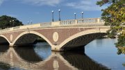 Weeks footbridge with its arches reflected in calm water under a blue sky.