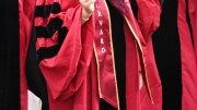 Close-up of a graduate's arm in a red robe with "Harvard" sash during a ceremony.
