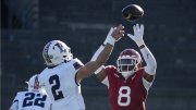 Harvard football player in red attempts to block a pass from a Penn player in white during a game.