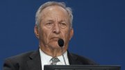 Lawrence Summers in a suit  at a podium with a microphone, looking serious.