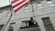 John Harvard statue beneath a large American flag outside of University Hall