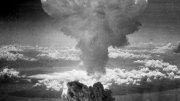 Black and white photo of a large mushroom cloud rising above the horizon.