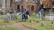 A student uses a shovel to clear debris and weeds from graves in a cemetery