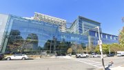 Modern glass building with reflective windows and trees, clear blue sky above.