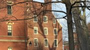 Historic red brick building with large windows and tree shadows in foreground.