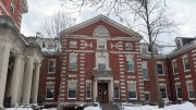 Brick building with classical architecture, surrounded by snow and bare trees.