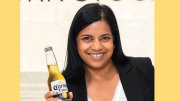 A woman in a black blazer holds a bottle of beer.
