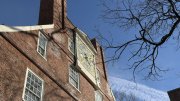 Brick building with a large clock and tree branches against a clear blue sky.