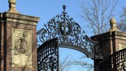 Wrought iron gates with ornate design, framed by brick pillars against a clear blue sky.
