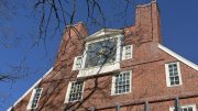 Massachusetts Hall under a clear blue sky, showcasing a prominent clock and large windows.