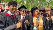 Three joyful graduates in caps and gowns celebrate together outdoors.