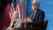 Two figures sitting against an American flag having a conversation at Harvard Kennedy School