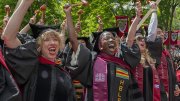 Graduates celebrate with joy, wearing caps and gowns, in a vibrant outdoor setting.