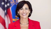 Rochelle Walensky in a red blazer with short dark hair, standing in front of flags.