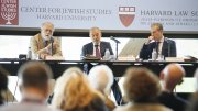 Three speakers at a panel discussion in front of an audience, with Harvard branding.