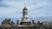 Harvard University tower with a red and gold dome against a blue sky.