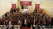 Graduating class posing together in a Harvard ceremony, wearing caps and gowns.
