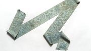 A long, patterned fabric ribbon in shades of blue and green, draped on a white background.