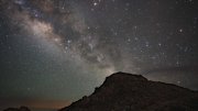 Star-filled night sky with the Milky Way arching over a rocky silhouette.