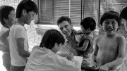A group of children interacts with an adult man, some laughing and smiling.
