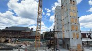 Construction site featuring tall concrete structures, cranes, and a blue sky with clouds.