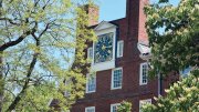 Massachusetts Hall at Harvard Red brick building with a large clock on top, surrounded by green trees.