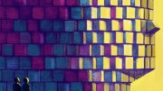 Two figures stand before a large, colorful pixelated face against a yellow background.