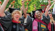 Graduates in caps and gowns celebrate joyfully, raising their hands in excitement.