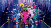 A vibrant group of dancers in colorful outfits poses on a stage with shiny decorations.
