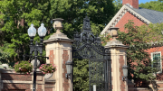 Morgan gate with brick pillars, surrounded by greenery and historic architecture.