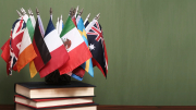 Assorted national flags arranged on a stack of books against a green background.