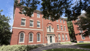 Red brick building with large windows and greenery, set against a bright blue sky.