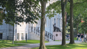 University Hall with steps and the John Harvard statue, surrounded by trees and a grassy lawn.