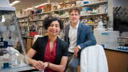 Two laboratory researchers, one seated and one standing, in a scientific lab with equipment.