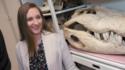 Smiling woman stands beside a large skull in a display cabinet.