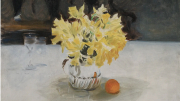 A vase of yellow flowers on a table next to an orange and a glass.