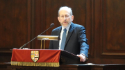 Man wearing a suit stands at a podium and speaks into a microphone.