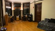 A large dorm room with desk, bed, lamps, and quarantine necessities, including bottled water, masks, and sanitizing supplies.