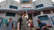 Muhammad Farid Abdul Rahman, Jimmy Potter, and Gitangu stop outside after surveying a public toilet building and interviewing the desk attendant about the bathroom’s cost and cleaning schedule.