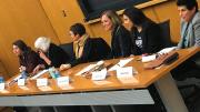 Six women sit at a table at the front of an auditorium. 