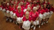 Photo of a cheerleader group composed of elderly women, all in red tops and white skirts, with pompoms