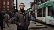 Stephen Gray stands on city sidewalk with street car passing by on right