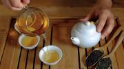 Hands pouring steeped golden-colored tea from a ceramic pot