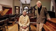 An older couple standing in a large room filled with pianos
