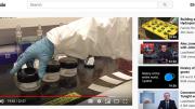 A human arm wearing a white goat and rubber glove in a lab setting handles three containers of lab chemicals