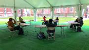Students gather in desks under a tent, a pilot of outdoor instruction for performance-based courses